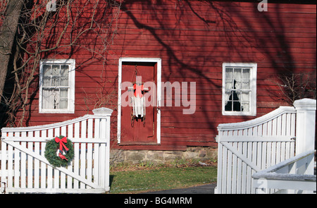 Eine Einfahrt Tor hat eine Weihnachten Kranz hängt es und die Tür des Hauses einen Vintage Schlitten mit einem Bogen als Dekoration hat. Stockfoto