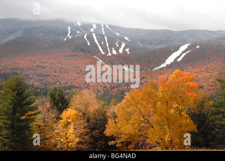 Herbst-Bäume in leuchtenden Farben steht im Vordergrund, als neue Schnee liegt auf den Skipisten von Mt. Ellen Sugarbush Resort in Fayston Stockfoto