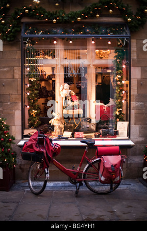 Ein Mitarbeiter der britischen Post Fahrrad vor einem Schaufenster dekoriert für Weihnachten in Cambridge, England Stockfoto