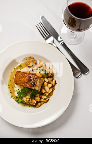 Ein Stück Schweinebauch serviert mit Bohnen und ein Glas Rotwein. Das Essen im Restaurant. Stockfoto