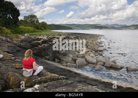 Frau saß auf dem Strand, Blick auf Lamlash aus Kingscross Punkt, The Isle of Arran, Schottland, Juni 2009 Stockfoto