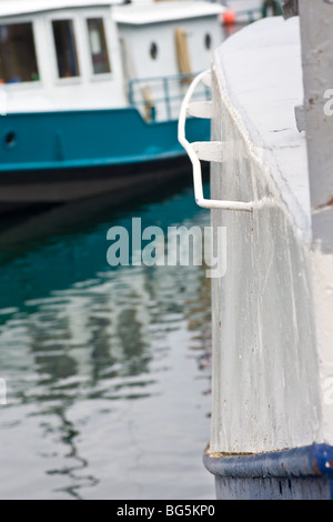 Die Ecke von einem alten Boot, zeigt die Textur des es ist gemalt Rumpf mit einem anderen Boot und Spiegelungen im Wasser hinter. Stockfoto