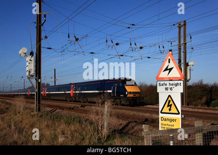 82207 beschleunigen Zug Overhead spannungsführende Leitungen Warnschild an unbemannten Schranke überqueren East Coast Main Line Peterborough Stockfoto