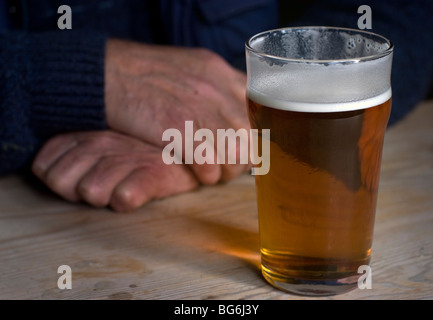 Pint bitter mit mans Hände hinter ruht auf geschrubbt Holztisch Stockfoto