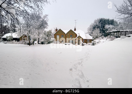 Spuren in den unberührten Schnee zu Landhaus umgeben von Bäumen Stockfoto