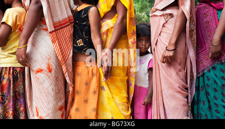 Starrte indische Mädchen stehen in zwischen Müttern tragen bunte Sari's in einer Warteschlange. Andhra Pradesh, Indien Stockfoto