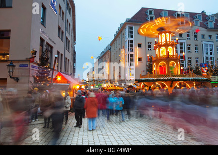 Der lebhafte Weihnachtsmarkt mit Besuchern in der Abenddämmerung bietet ein festliches Karussell und Weihnachtsbeleuchtung in Dresden. Stockfoto