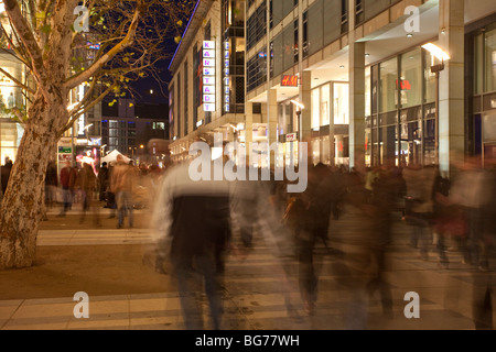 Unscharfe Bewegungen der Fußgänger in der Prager Straße, Dresden, geschmückt mit festlichen Lichtern in der Weihnachtsnacht. Stockfoto