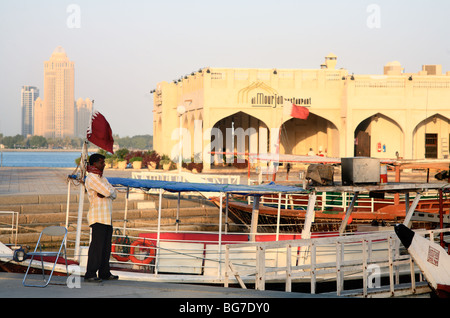 Ein Fährmann wartet für den Handel an der Corniche in Doha, Katar, während die untergehende Sonne die Gebäude rosa malt. Stockfoto