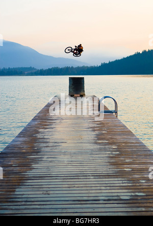 Ein Freestyle-Mountain-Bike-Fahrer Praktiken risikoreiche Tricks aus einer Rampe springen auf einem Dock in einen See. Stockfoto