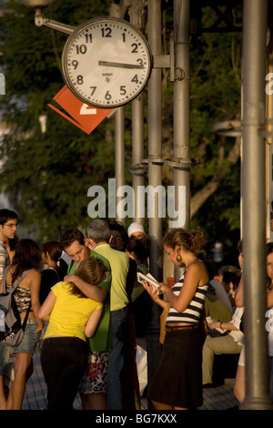 ROMANTISCHE BAHNHOFSSZENE: Ein junges Paar küsst sich und eine Frau, die ein Buch liest, wartet auf den Zug am Bahnhof Sitges in der Nähe von Barcelona Spanien Stockfoto