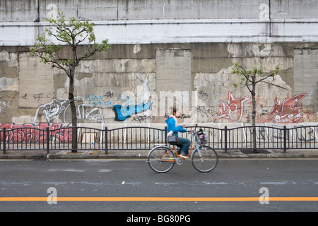 Junge Frau Reiten Fahrrad auf der Straße vor Graffiti, Osaka, Japan. Stockfoto