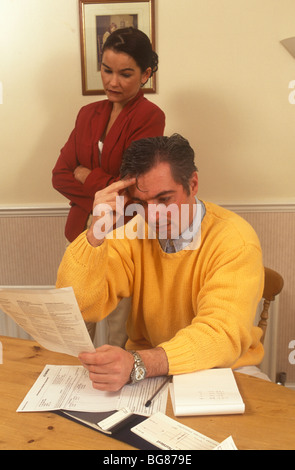 Mann sucht ängstlich und gestresst über Rechnungen mit seinen ethnischen Partner im Hintergrund schauen ängstlich Stockfoto