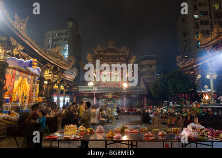 Lungshan Tempel, historischen buddhistischen und taoistischen Tempel, Anbeter, Essen und Blumen Angebote bei Nacht gesehen, Wanhua District, Taipei City, Taiwan Stockfoto