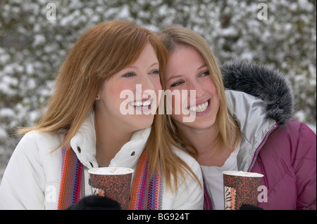 Zwei Mädchen trinken heiße Schokolade oder Kaffee draußen im Schnee Stockfoto