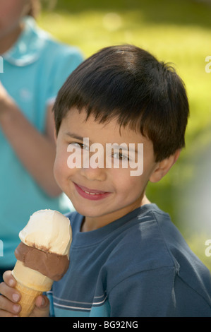 Junge hält einen Schokolade und Vanille-Eiscreme-Kegel außerhalb mit Mädchen im Hintergrund Stockfoto