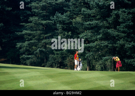 Golfer Abschlag auf einem Golfplatz, während Caddy Uhren Stockfoto