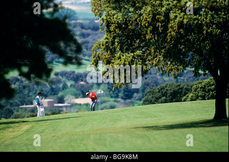 Golfer Abschlag auf einem Golfplatz, während Caddy Uhren Stockfoto
