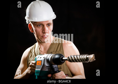 Der Bauherr in einem Schutzhelm hält die professionelle Puncher-Hammer mit einem Bohrer des großen Durchmessers Stockfoto