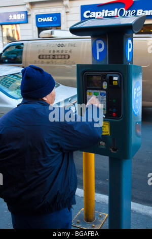 Asiatischer Mann Fütterung eine solar betriebene Parkuhr in Chinatown in New York City Stockfoto