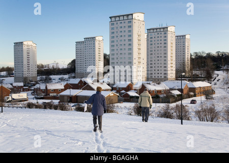 Menschen gehen über den Schnee in Sunderland, England. Das Hochhaus Gilley Law Wohnsiedlung können im Hintergrund zu sehen. Stockfoto