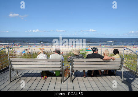 Menschen sitzen auf Bänken neben hölzernen Fußweg auf Sanddünen entlang der baltischen Küste in Swinoujscie, Polen Stockfoto