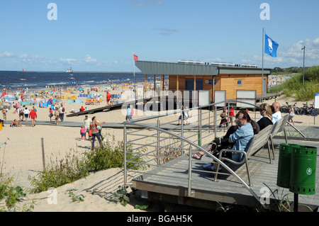 Menschen sitzen auf Bänken neben hölzernen Fußweg auf Sanddünen entlang der baltischen Küste in Swinoujscie, Polen Stockfoto