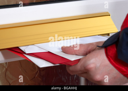 Postmans Hand schieben Briefe und Karten in den Briefkasten eines Hauses im Vereinigten Königreich Stockfoto