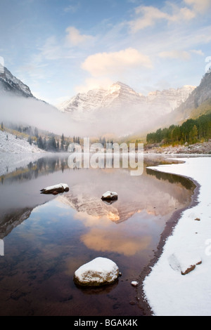 Maroon Bells (im Hintergrund) im Morgennebel mit See, Schnee und Eis Bildung im Vordergrund. Stockfoto