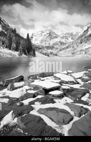 Maroon Bells im Hintergrund und großen Steinen mit Schnee an den Ufern des Sees. Bewölkten Himmel und schwarz / weiß Bild Stockfoto