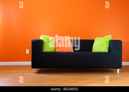 Zeitgenössische schwarze Couch gegen helle orange Wand in einem modernen Wohnzimmer Stockfoto