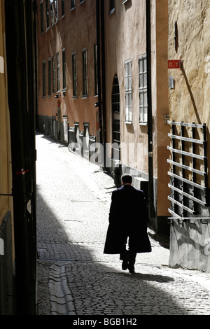 MAN IN DARK CAPE, BACKSTREET SILHOUETTE, STOCKHOLM: Ein Mann in einem dunklen cape in Silhouette geht durch die enge Kopfsteinpflasterstraße Gamla Stan Stockholm Schweden Stockfoto