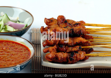 Eine Platte mit Chicken Satay serviert auf einer Platte und Bambus-Matte mit in Scheiben geschnittenen Zwiebeln, Gurken und eine Schüssel mit Soße Stockfoto