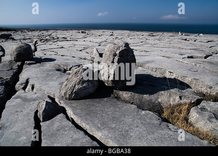 Irland, County Clare, Burren, Felsbrocken auf Kalkstein Pflaster Abschnitt in der Nähe von Black Head mit dem Atlantischen Ozean hinter. Stockfoto