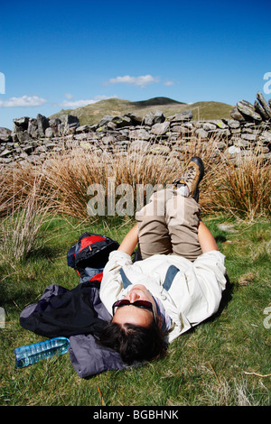 Weibliche Wanderer ausruhen und erstreckt sich in der Nähe von Fußweg am Ansatz bis zum Gipfel des Ortes fiel in der Nähe von Ullswater im Lake District Stockfoto