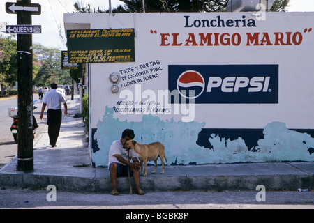 gemalte Werbung auf Wand und Mann mit Hund sitzt auf der Straße - Cozumel - Mexiko Stockfoto