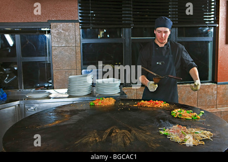 Koch mit Utensilien durchführen, während der Zubereitung von Mahlzeiten im Mongolie World Famous hineinschütten Grillrestaurant in Whistler Village, B Stockfoto