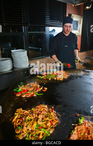 Koch mit Geschirr und Essen während der Zubereitung von Mahlzeiten im Mongolie World Famous hineinschütten Grillrestaurant in Whistler V Ausführung Stockfoto