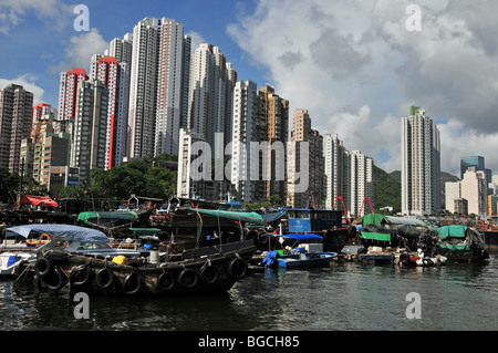 Sampan Hausboote vertäut unter einer wellenartigen Mauer des Hochhaus-Apartment-Türme an der Seite von Aberdeen Harbour, Hong Kong, China Stockfoto