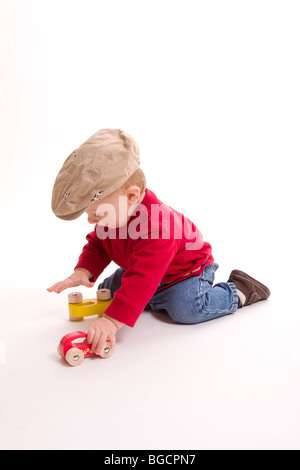 1 Jahr alt kleiner Junge tragen große Kappe spielt mit Spielzeugautos isoliert auf weiss Stockfoto