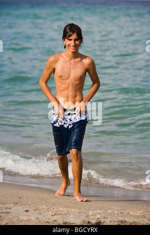 Teenager-Junge, der in Badehosen und am Strand läuft, lächelnd, Porträt. Stockfoto