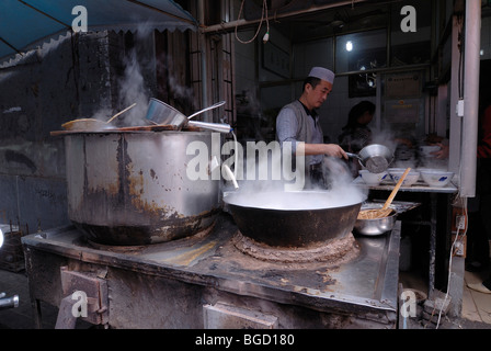 Muslimische Nudel Suppe Garküche mit einem muslimischen Koch und großen dampfenden Kesseln auf einem Eisenofen im muslimischen Viertel von Xian, Shaan Stockfoto