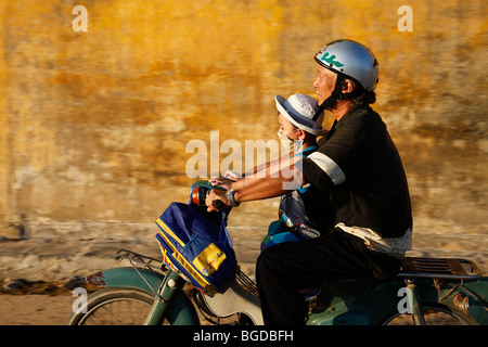 Vietnamesische Vater mit seinem Sohn auf seinem Motorroller mit einem Rucksack, Hoi an, Vietnam, Südostasien Stockfoto