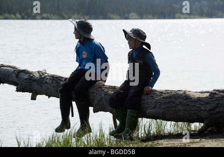 Im Urlaub, Geschwister, 12 Jahre altes Mädchen und 6 Jahre alten Jungen, sitzen auf einem Baumstamm, Teslin River, Yukon Territorium, Kanada Stockfoto