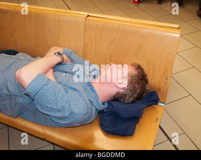 Gelangweilt Mann männliche Erwachsene Flugreisende schlafen auf harten Flughafen Sitze in Gatwick, Sussex, England, UK, Großbritannien Stockfoto