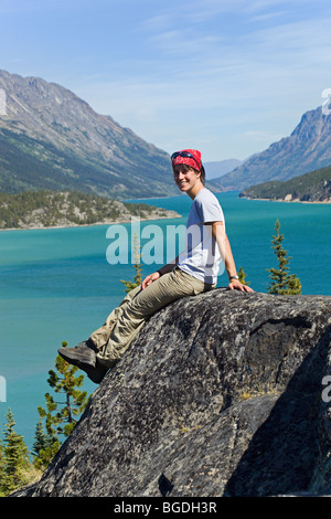 Junge Frau, Wanderer, Backpacker sitzt auf Felsen, Ruhe, Panorama, Blick auf Lake Bennett, historische Chilkoot Pass, Chi genießen Stockfoto