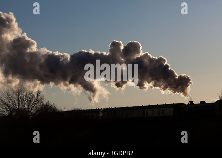 Eine Silhouette von einem Dampfzug verlässt Rauchwolken, da es einen Bahnhof zieht. Stockfoto