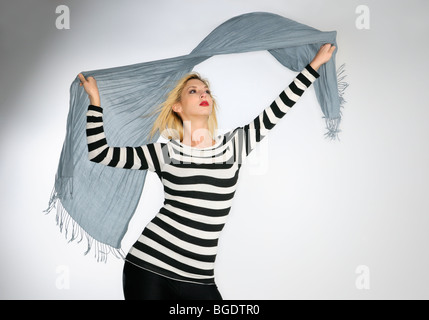 Junge Frau in gestreiften Oberteil winken einen Schal in den Wind auf weißem Hintergrund Stockfoto