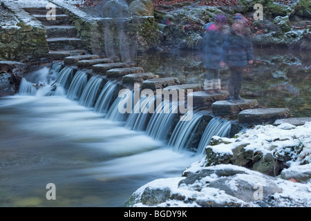 Menschen, die zu Fuß über Trittsteine über einen Fluss und kleinen Wasserfall im Tollymore Forest Park in Nordirland Stockfoto