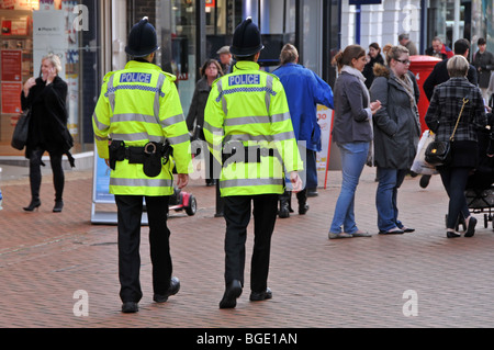 Polizeibeamte im Hintergrund sehen zwei ähnliche Polizisten zu Fuß auf Patrouille, die in der geschäftigen Einkaufsstraße in der Stadt Chelmsford Essex England spazieren Stockfoto